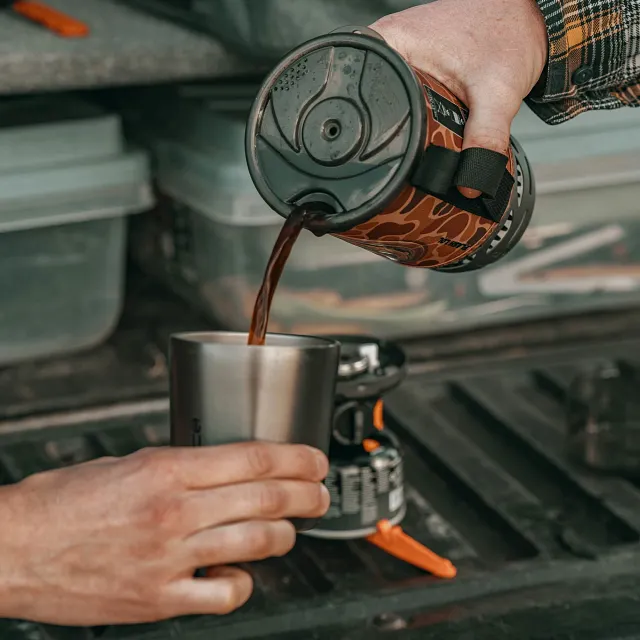 Pouring hot freshly made coffee from the Jetboil Flash 1.0L Fast Boil System in Duck Camo into mug to drink