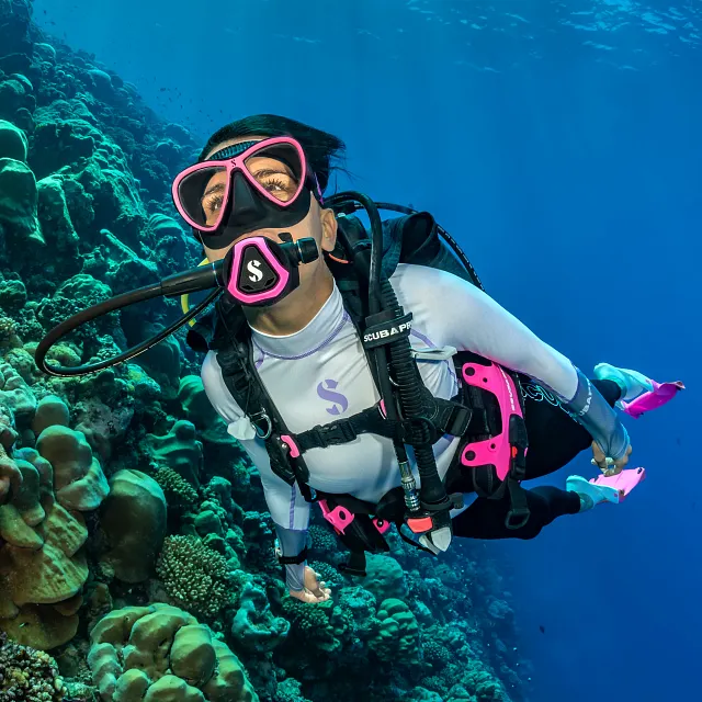 Duikster onder water die een C370‑duikregelaar met roze kleurframe gebruikt bij een koraalrif.