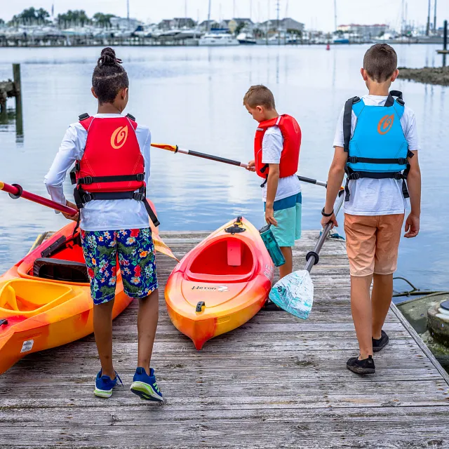 Children wearing Old Town Inlet Jr Youth Life Jacket and holding Carlisle paddles near kayaks