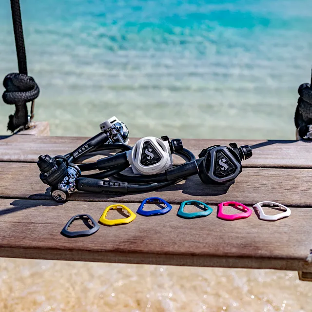 Systèmes de détendeur de plongée SCUBAPRO C370 présentés sur un ponton en bois au bord de la mer, avec des caches frontaux interchangeables de différentes couleurs disposés à l’avant.