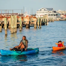 Woman pedaling in Old Town Ocean Kayak Malibu PDL towing child in Banzai kayak