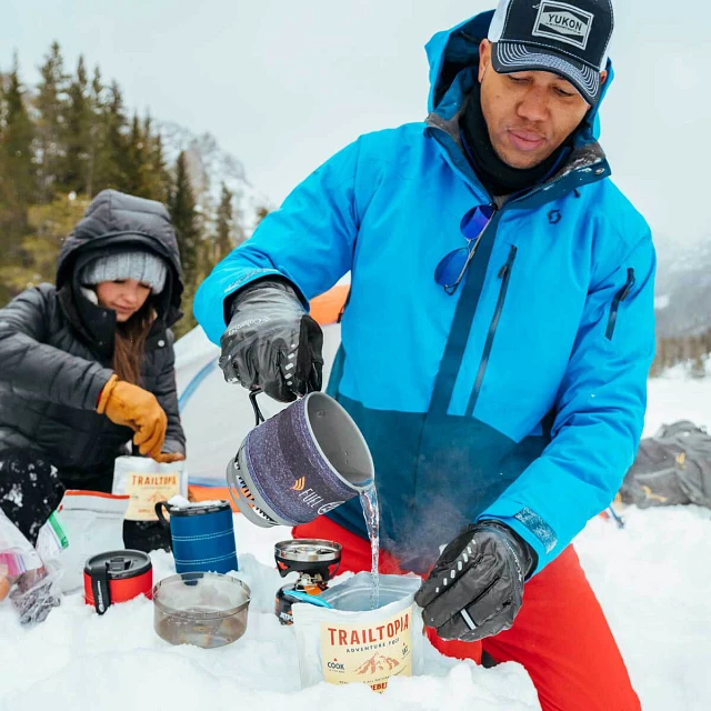 Man and Woman on a winter hike pouring water from the Jetboil MiniMo Cooking system to make a hot meal