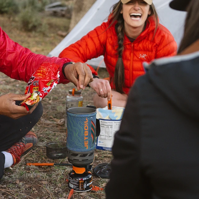 Friends gathered and adding noodles to Jetboil Flash 1.0L Cooking System Stove in Ocean Topo