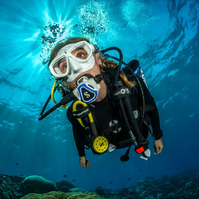 Taucherin unter Wasser mit einem C370‑Tauchatemregler mit blauem Farbrahmen, mit aufsteigenden Luftblasen und einfallendem Sonnenlicht.