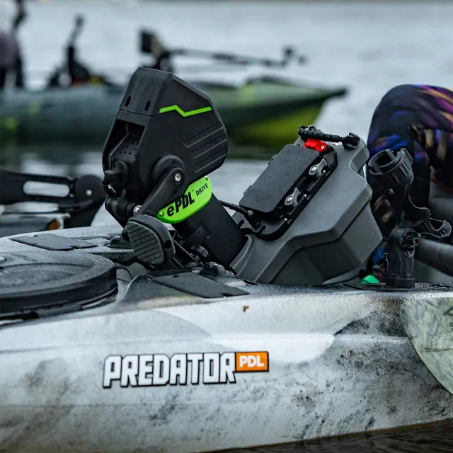 An Old Town kayak with a white and gray camouflage hull features a black and green ePDL Drive pedal system, a gray console with a black top panel and red lever, and a black rod holder.
